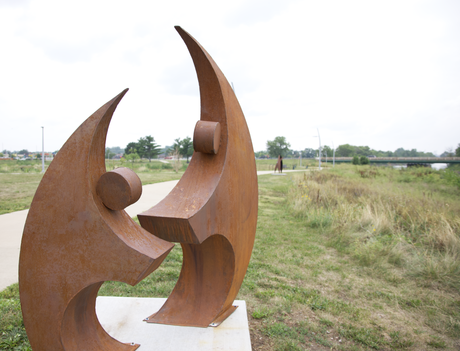 A steel sculpture that looks like two people holding arms out is shown. 